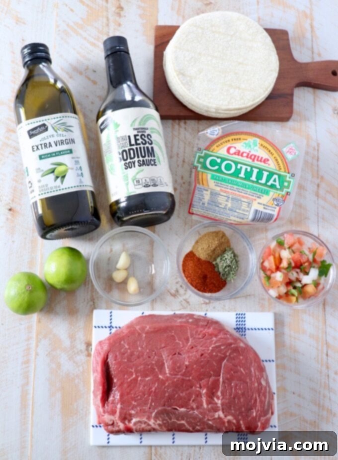 A flat lay image displaying all the fresh ingredients required to make chili lime steak tacos, including steak, spices, lime, garlic, tortillas, and cilantro.