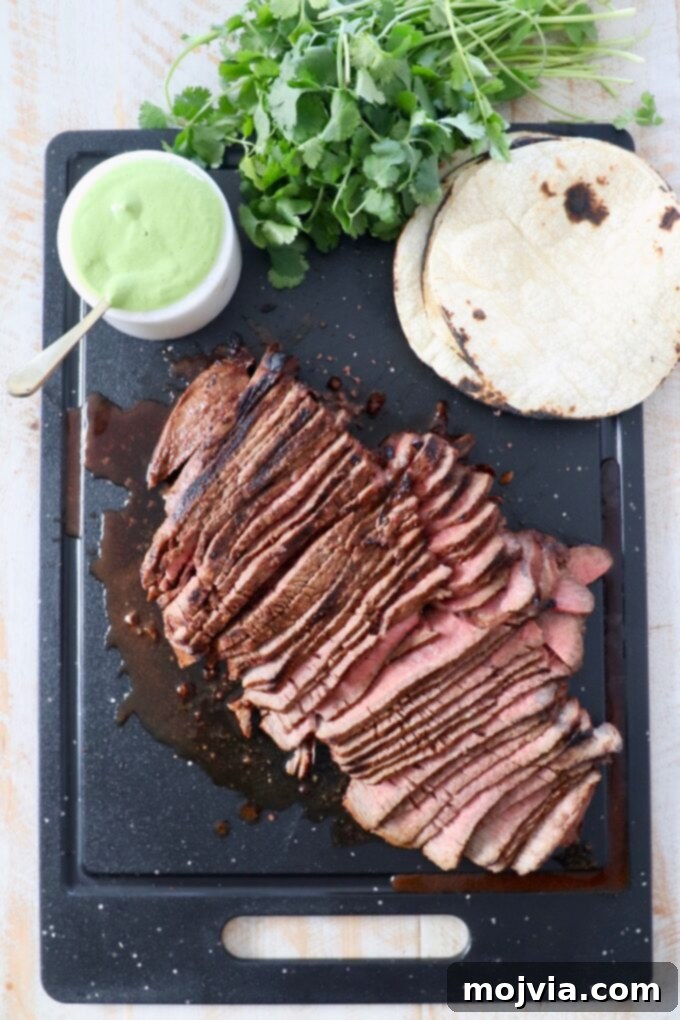 Sliced chili lime steak resting on a cutting board, alongside warm tortillas and creamy cilantro sauce.