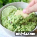 hand dipping tortilla chip into bowl of guacamole