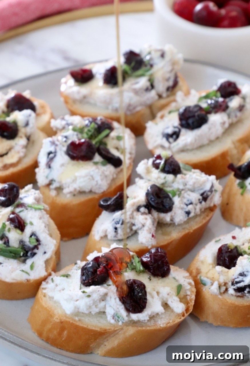 Creamy Goat Cheese and Tart Cranberry Crostini 2 honey drizzling over cranberry goat cheese crostini on a plate