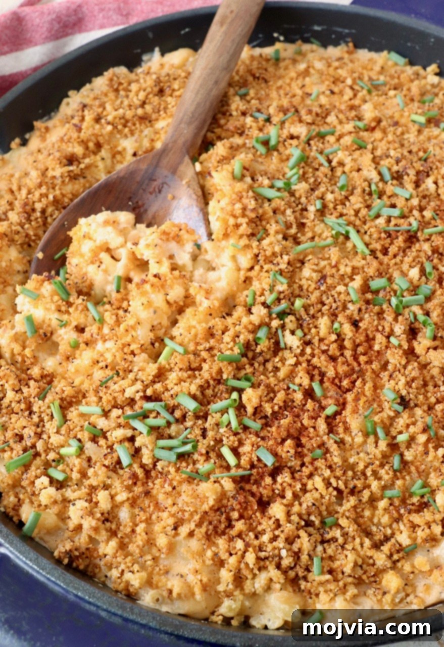 Velvet Smoke Mac 18 serving spoon in skillet of smoked mac and cheese topped with chopped chives