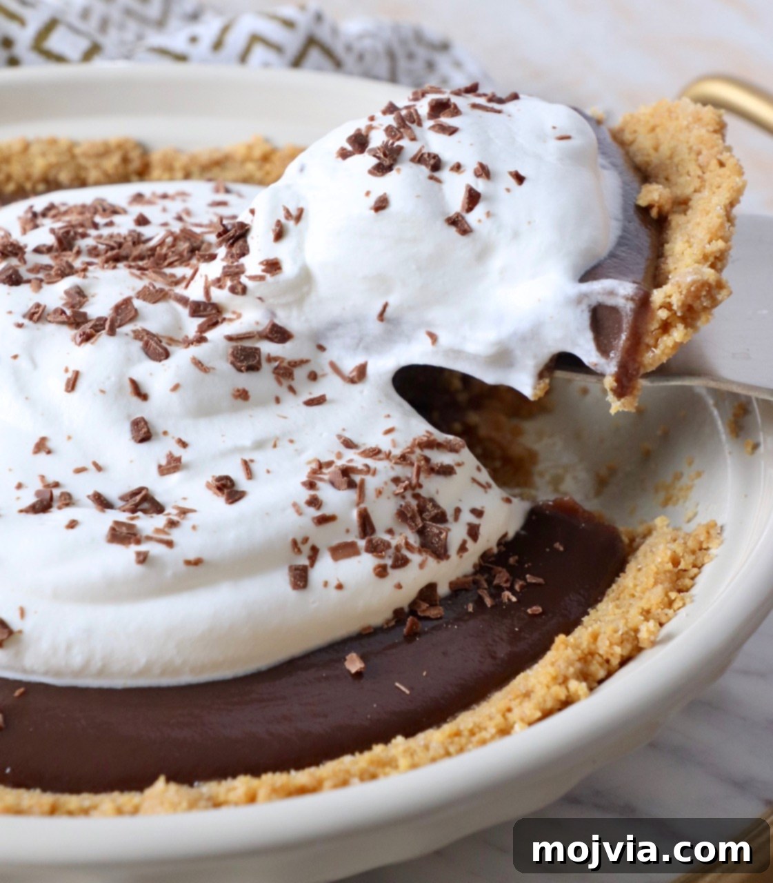 A perfect slice of Meme's famous homemade chocolate pie being lifted from the pan, revealing its rich chocolate filling, golden graham cracker crust, and a generous topping of fresh whipped cream, ready to be enjoyed as the ultimate dessert.