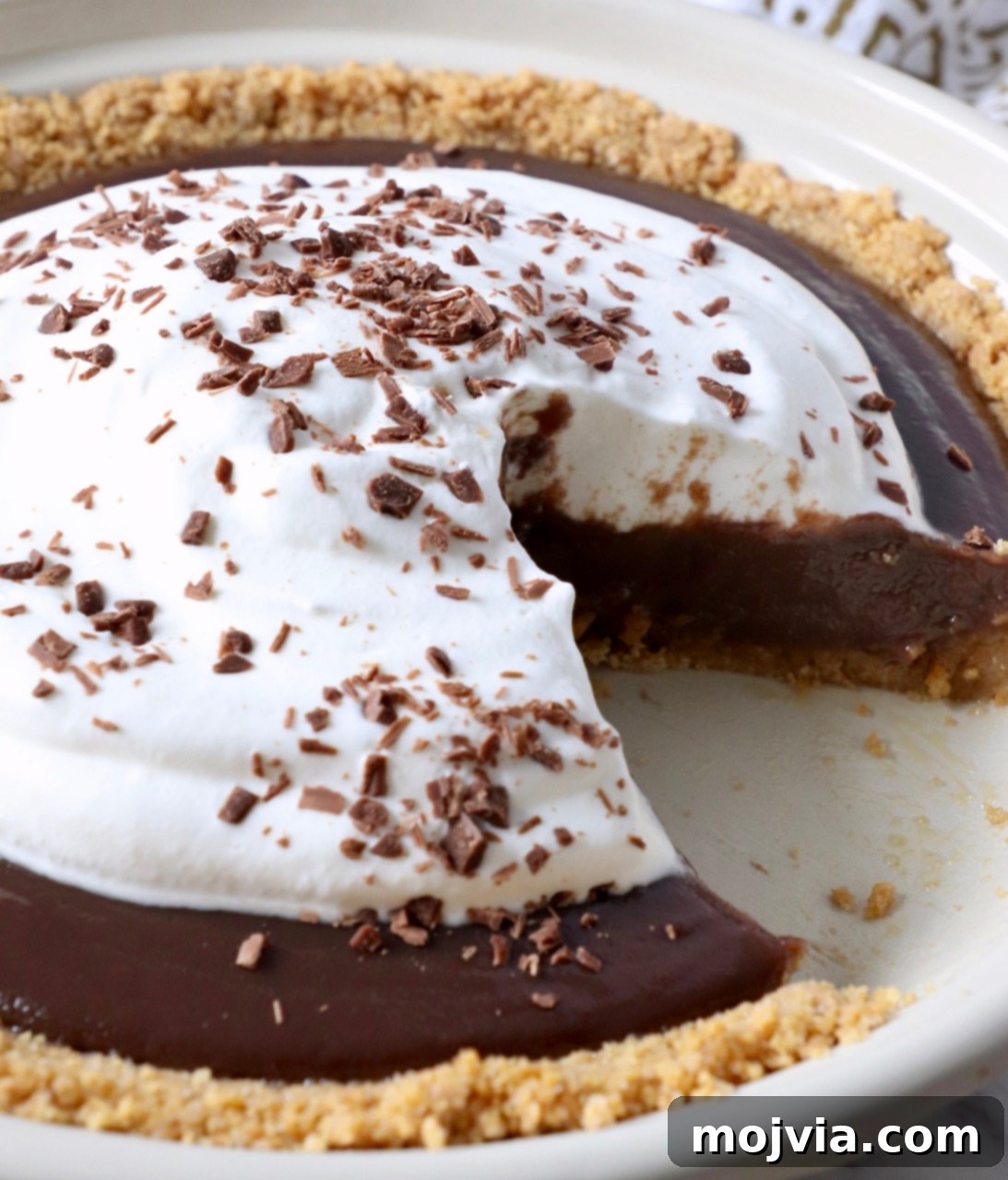 A tantalizing slice of Meme's easy homemade chocolate pie, complete with a generous dollop of whipped cream, removed from the full pie, showcasing its perfect layers and creamy texture.