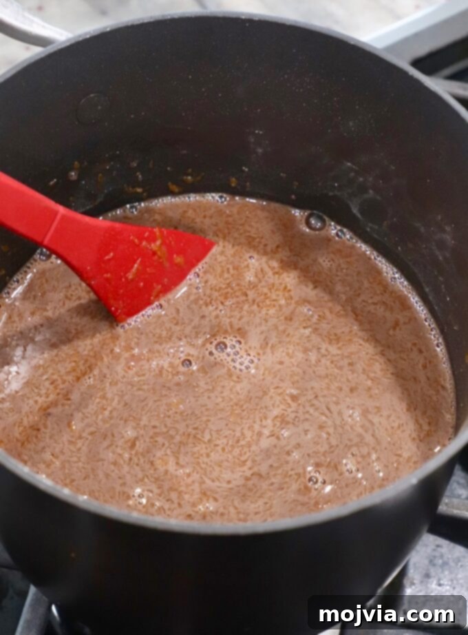 A red spoon continuously stirring the chocolate pie filling in a saucepan over medium heat as it begins to thicken.