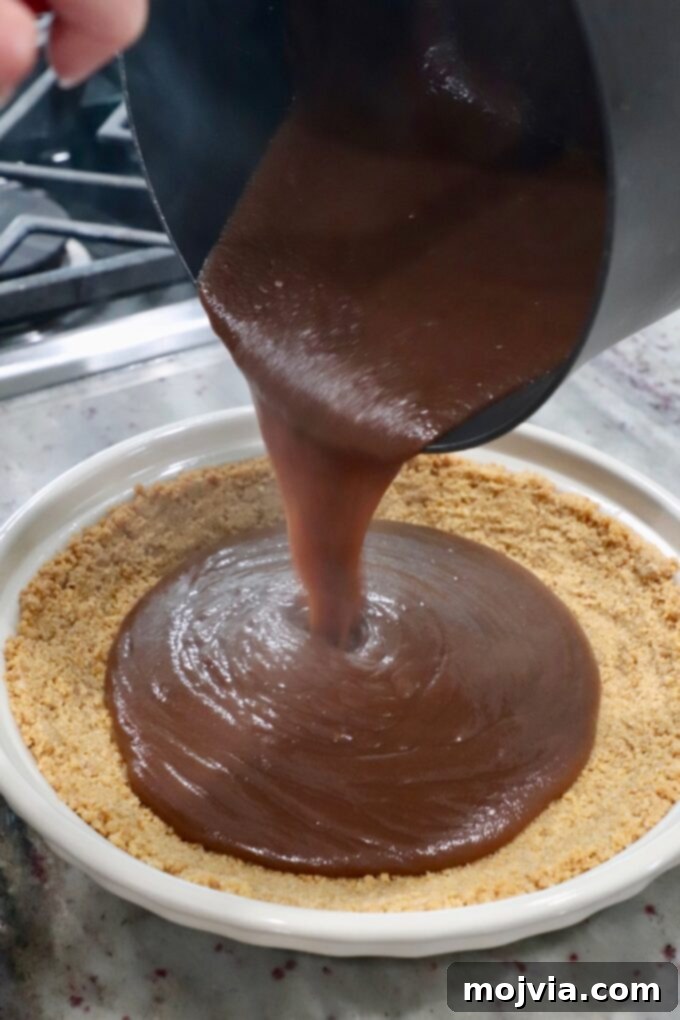 Pouring the warm, glossy chocolate filling into the baked graham cracker pie crust.