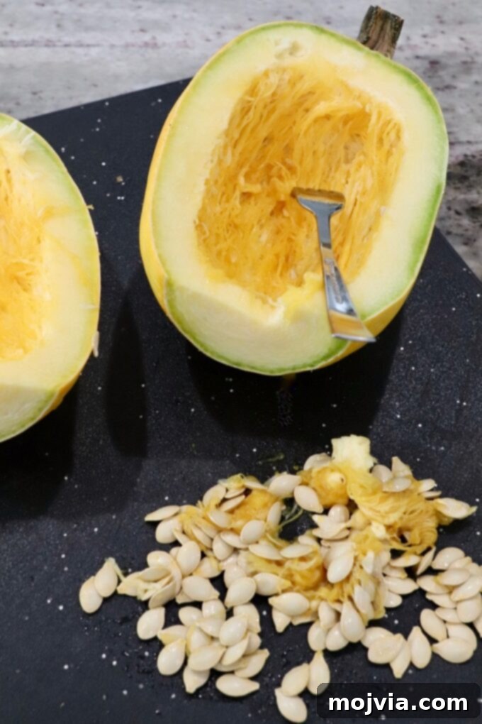 spaghetti squash cut in half on cutting board, with seeds removed on the side of the board