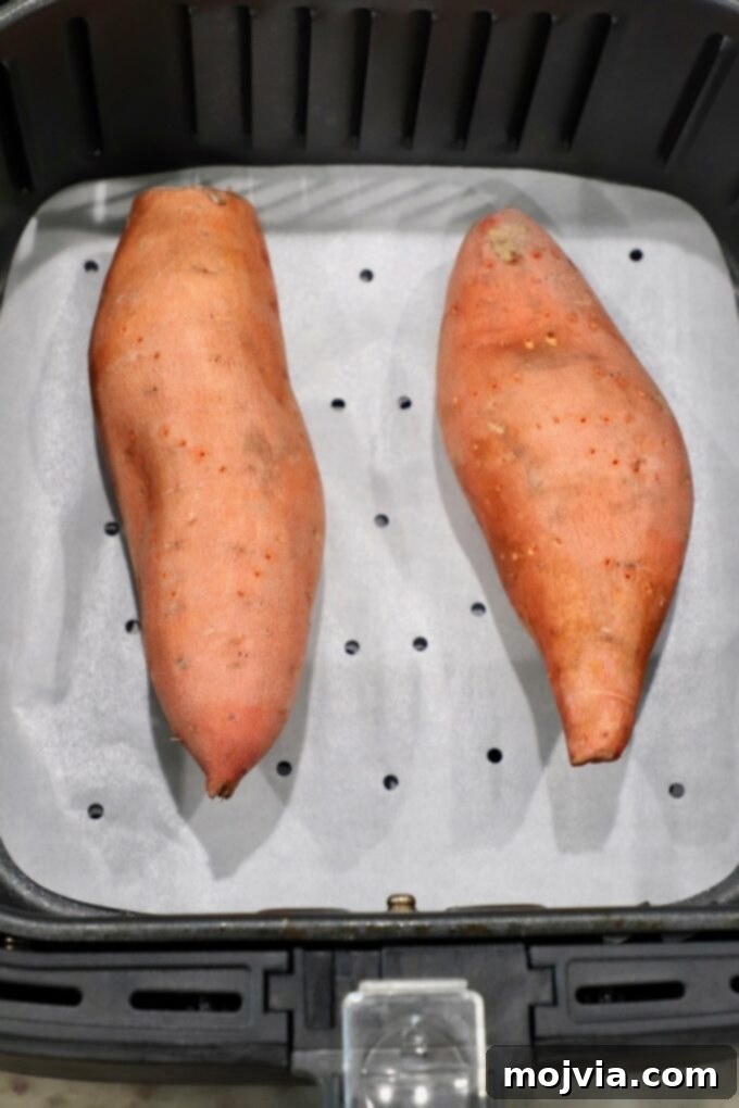 Sweet Potato Perfection Every Time 6 uncooked sweet potatoes resting in an air fryer basket, ready to cook
