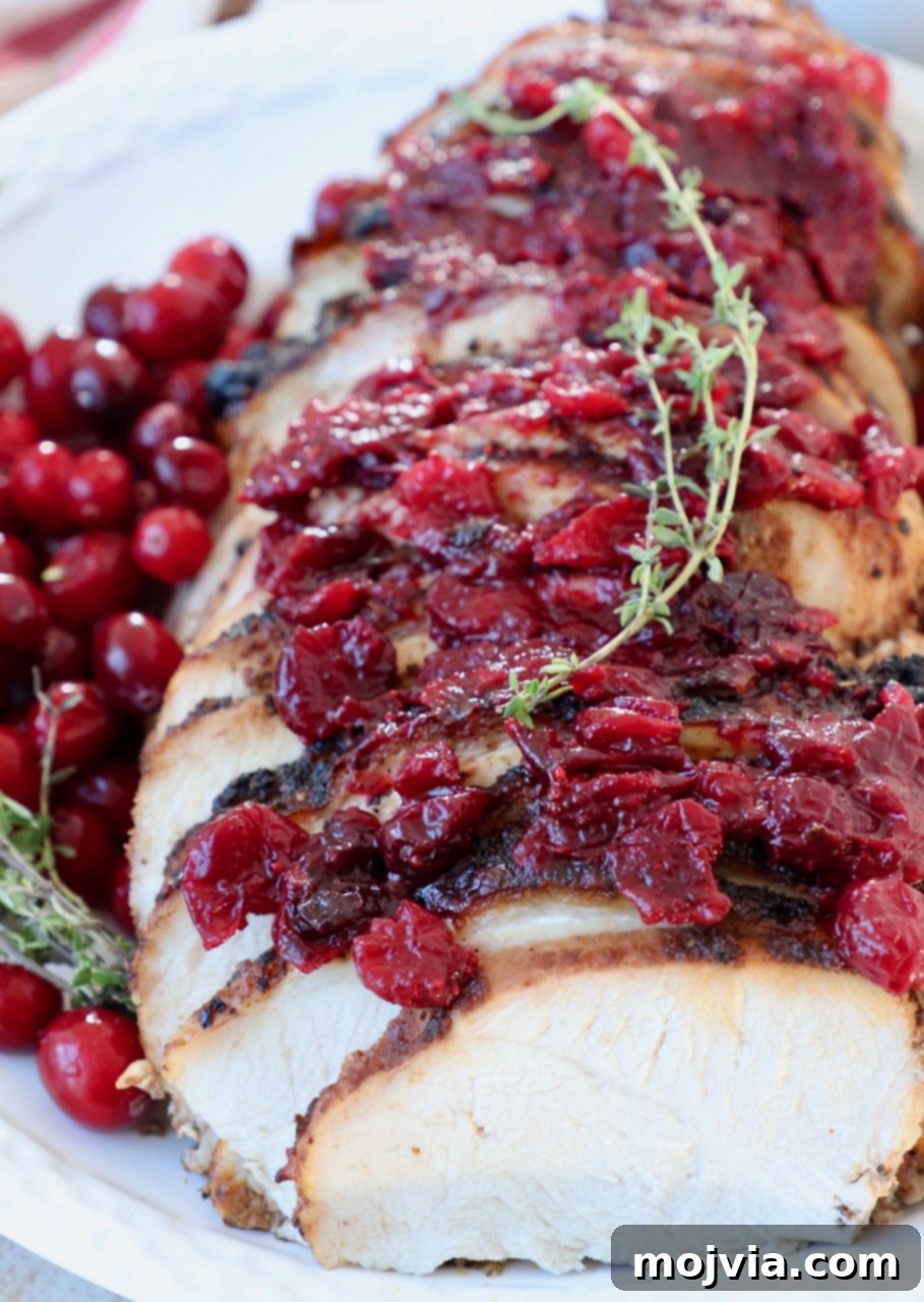 Sliced cranberry glazed turkey breast on a platter, garnished with fresh cranberries and thyme.