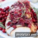 Sliced turkey breast covered with cranberry sauce and fresh thyme sprigs on white plate
