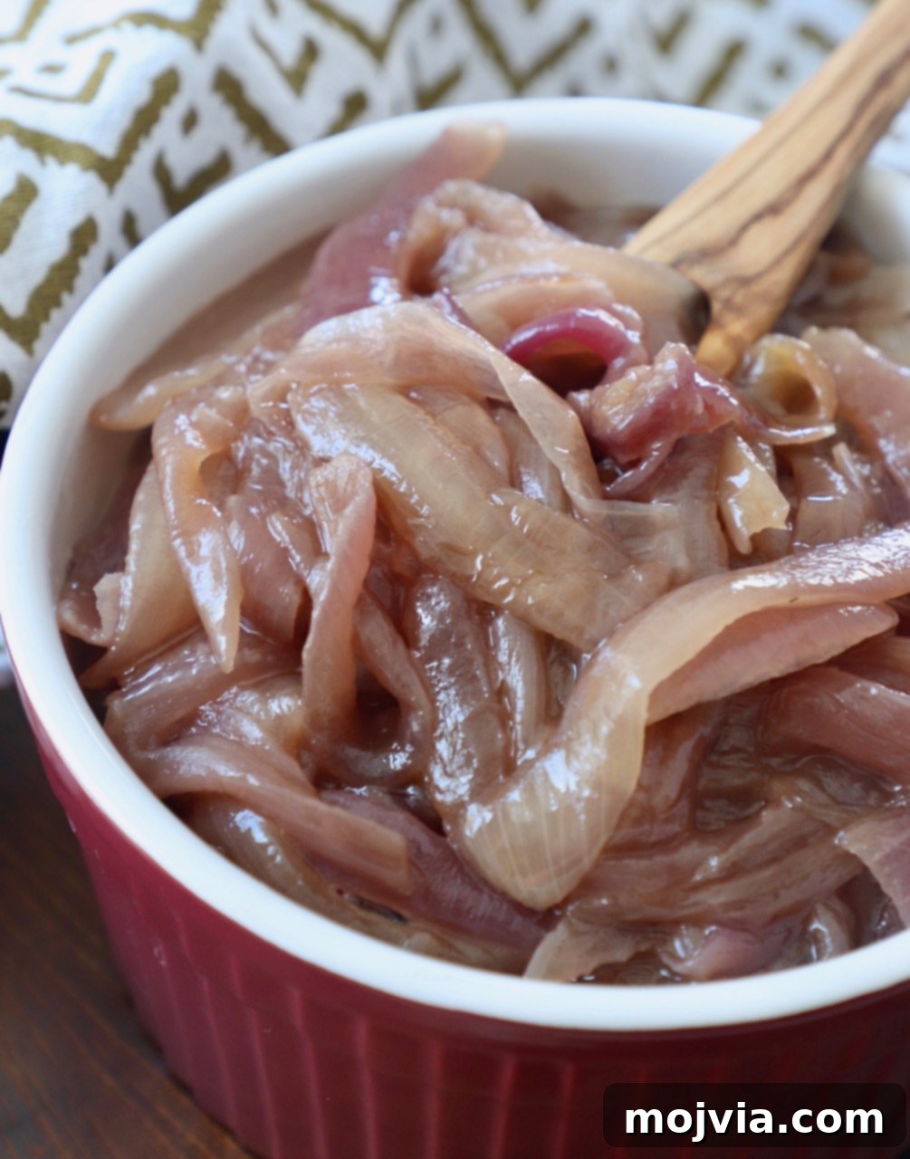 Crafting Irresistible Caramelized Onions 14 A vibrant red bowl filled with glistening caramelized onions, featuring a small wooden fork for serving.
