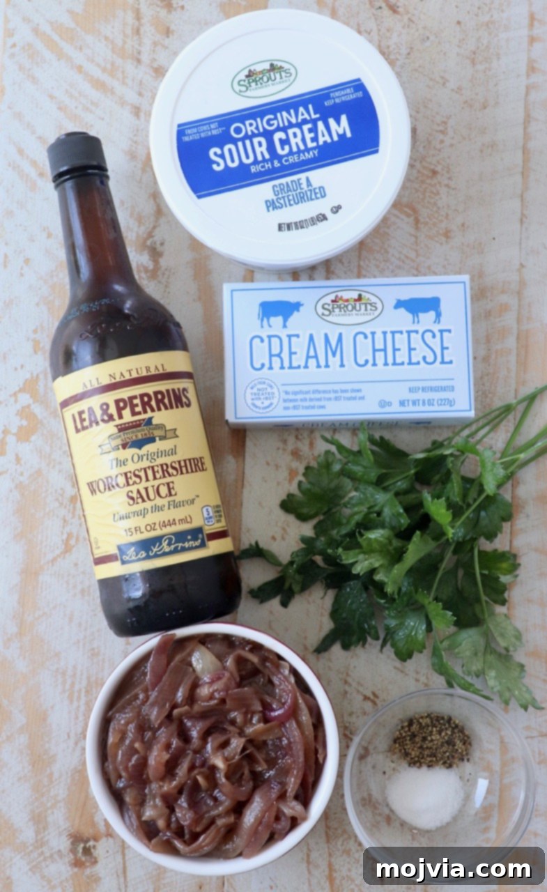A collection of fresh ingredients laid out for making French onion dip, including sour cream, cream cheese, fresh parsley, and a bowl of caramelized onions.