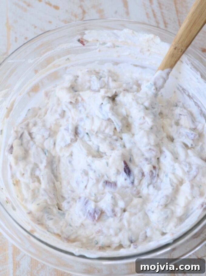 The French onion dip is fully mixed in a glass bowl, ready to be served or chilled, with a spatula resting inside.