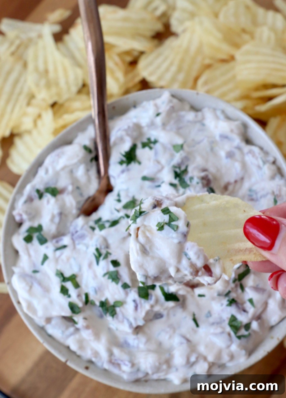 A hand dipping a wavy potato chip into a bowl of creamy French onion dip, highlighting its perfect texture.