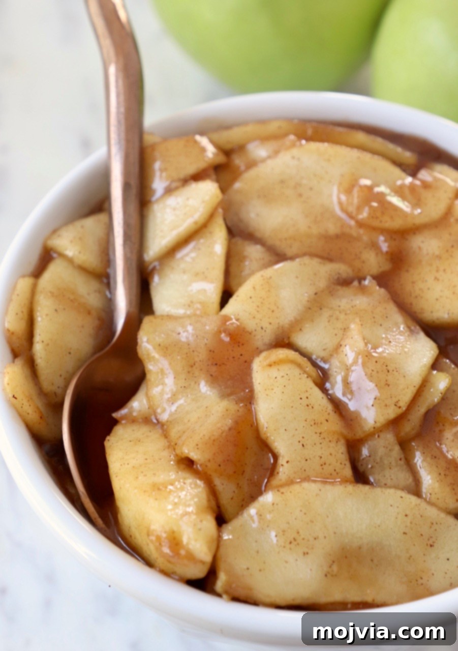 A generous serving of apple pie filling in a white bowl, with a spoon nestled inside, ready to be enjoyed.
