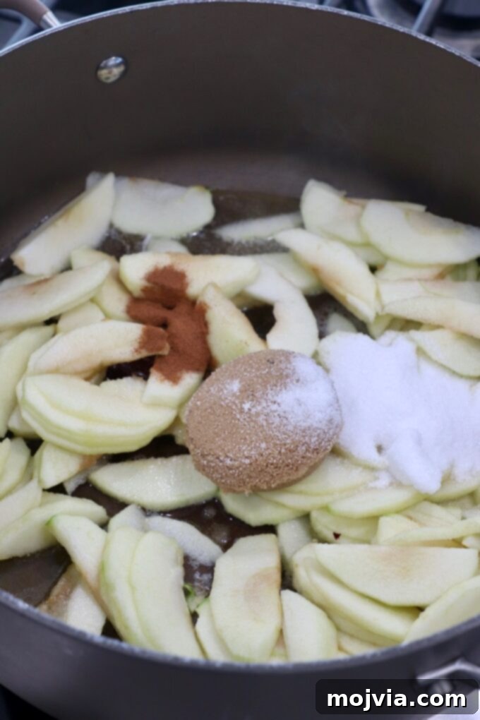 Apple slices cooking in a large skillet with sugar and cinnamon, creating an aromatic mixture.