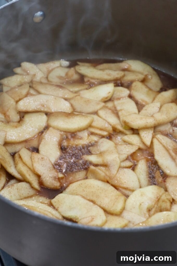 Cooked apples simmering in a skillet, now thickened into a luscious pie filling.