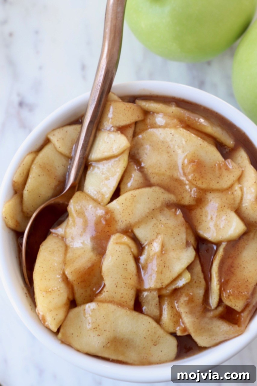 A beautiful white bowl filled with finished apple pie filling, accompanied by a elegant copper spoon.