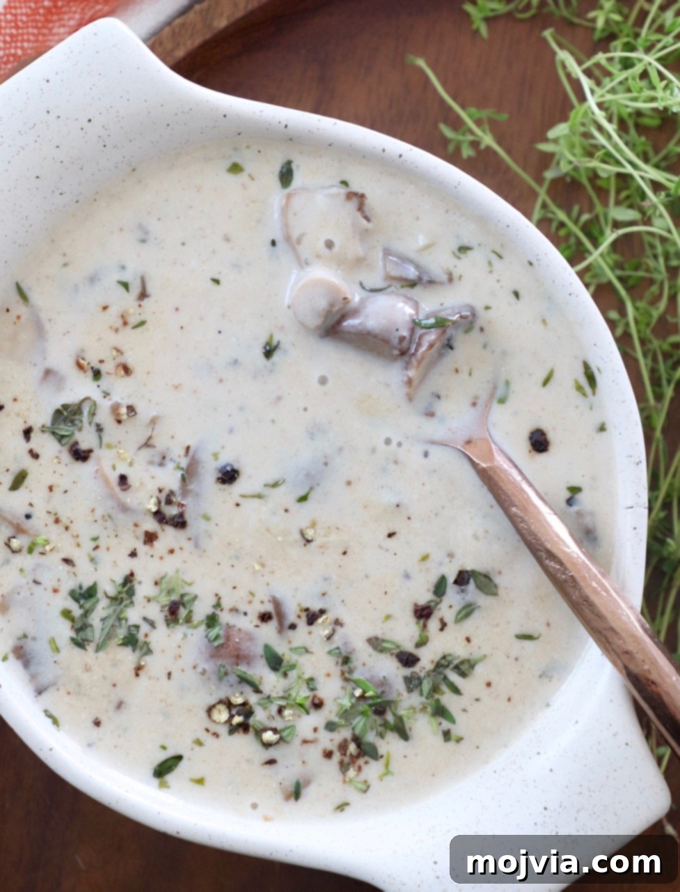 Velvety Mushroom Delight 2 A bowl of creamy homemade mushroom soup with a spoon, garnished with fresh herbs.