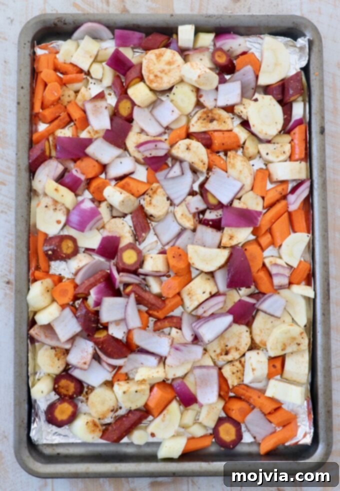 Earthy Harvest Roast 4 Uncooked diced root vegetables, including carrots, parsnips, and onions, spread out on a parchment-lined baking sheet.