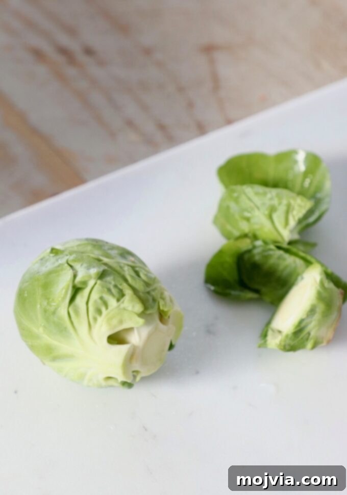 Shredding Brussels Sprouts Made Simple 4 A Brussels sprout on a cutting board with its tough stem and loose outer leaves already removed, showcasing the prepped vegetable.