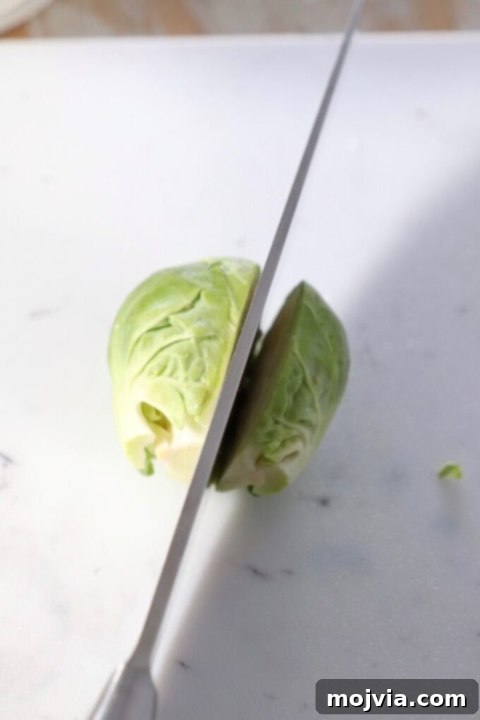 Shredding Brussels Sprouts Made Simple 5 A sharp knife precisely slicing a Brussels sprout in half lengthwise on a cutting board, a crucial step for manual shredding.