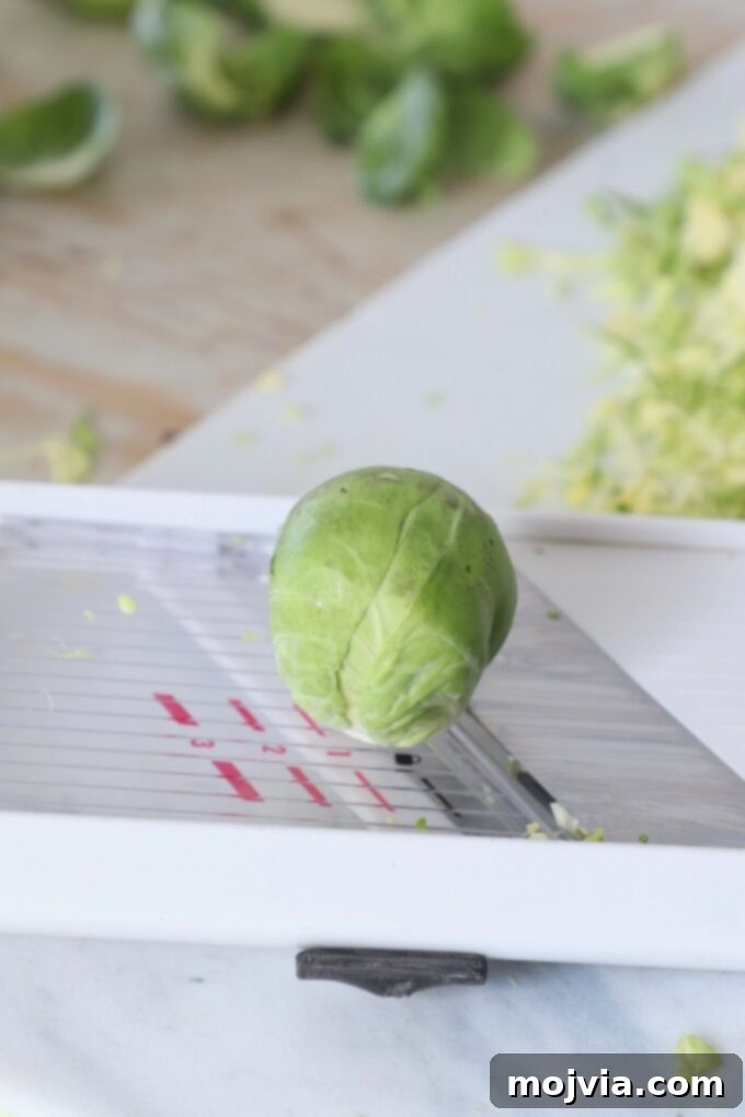 Shredding Brussels Sprouts Made Simple 7 A whole Brussels sprout positioned on a mandoline slicer, ready to be pushed across the blade for shredding.