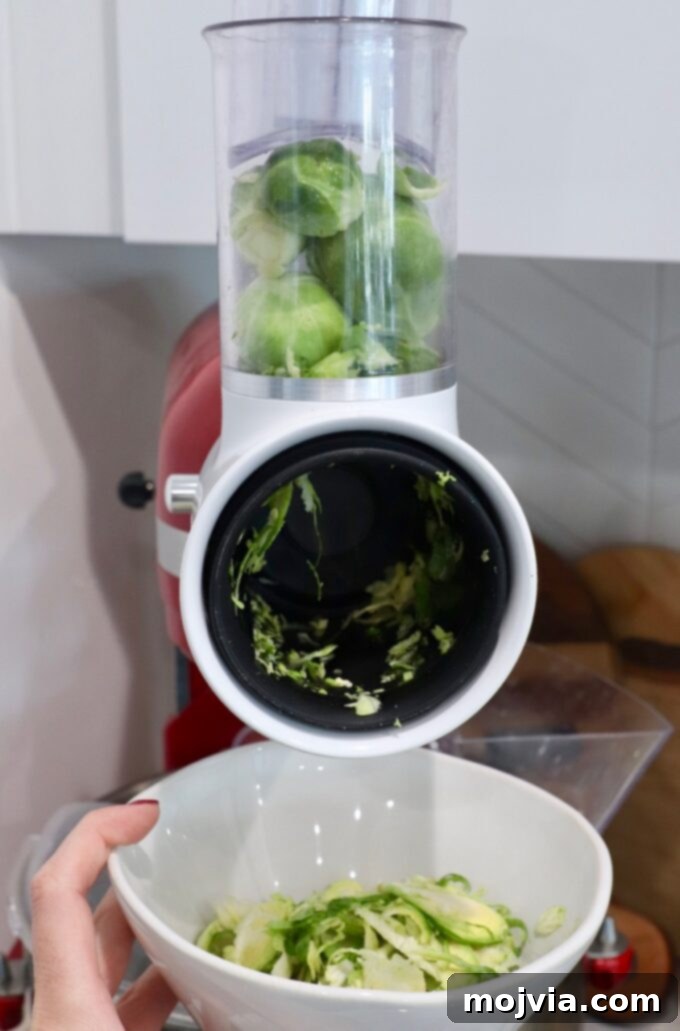 Shredding Brussels Sprouts Made Simple 9 Brussels sprouts loaded into the feed tube of a KitchenAid mixer with a grater attachment, showing the setup for automated shredding.