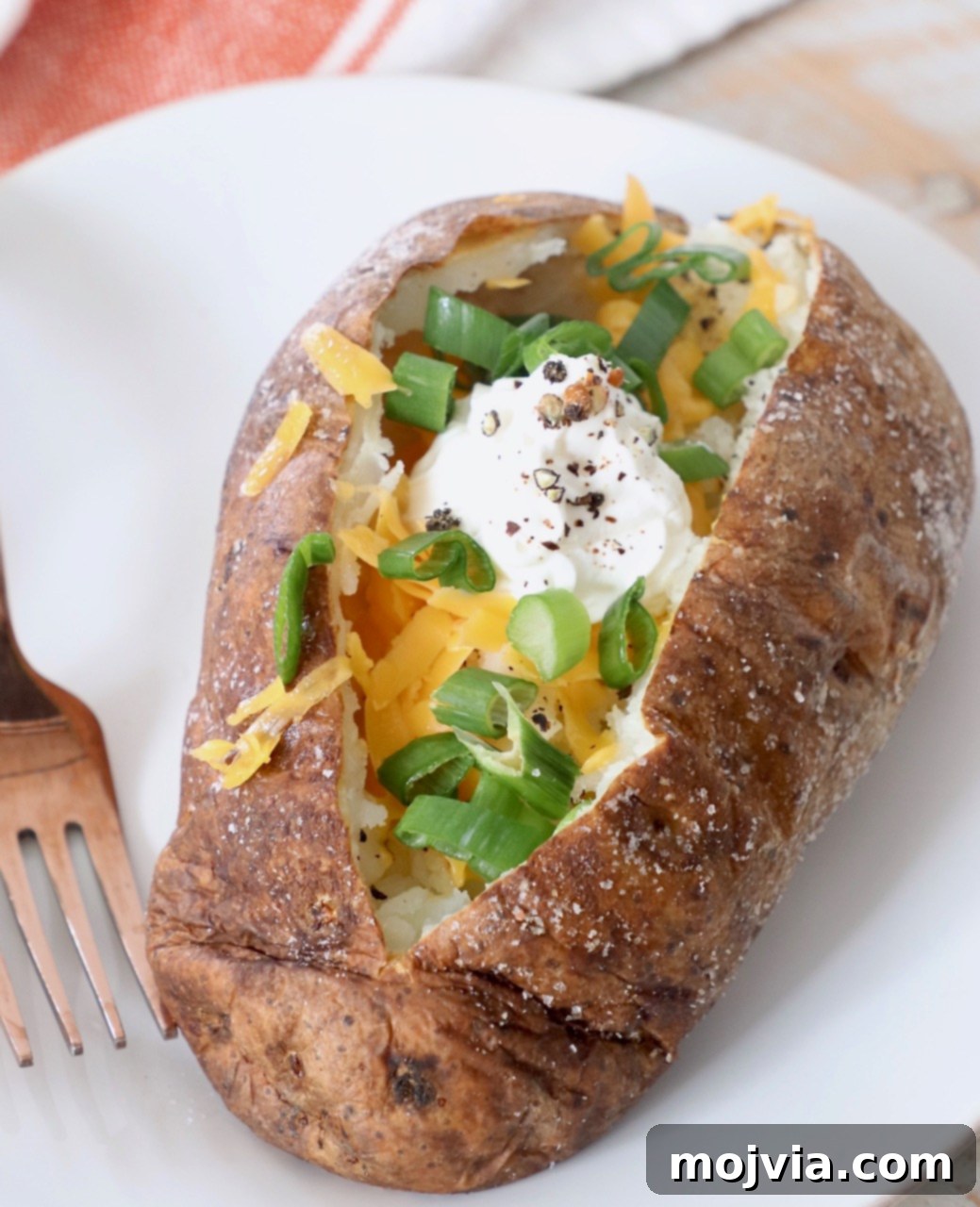 Crispy Air Fryer Baked Potatoes 2 baked potato on plate filled with diced green onions, cheese and sour cream