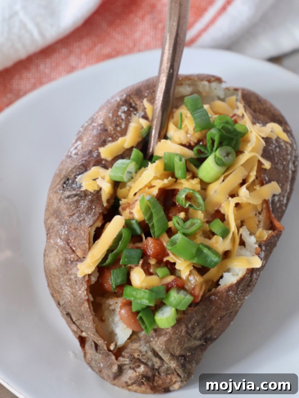 Crispy Air Fryer Baked Potatoes 5 baked potato on plate, filled with chili, shredded cheese and diced green onions
