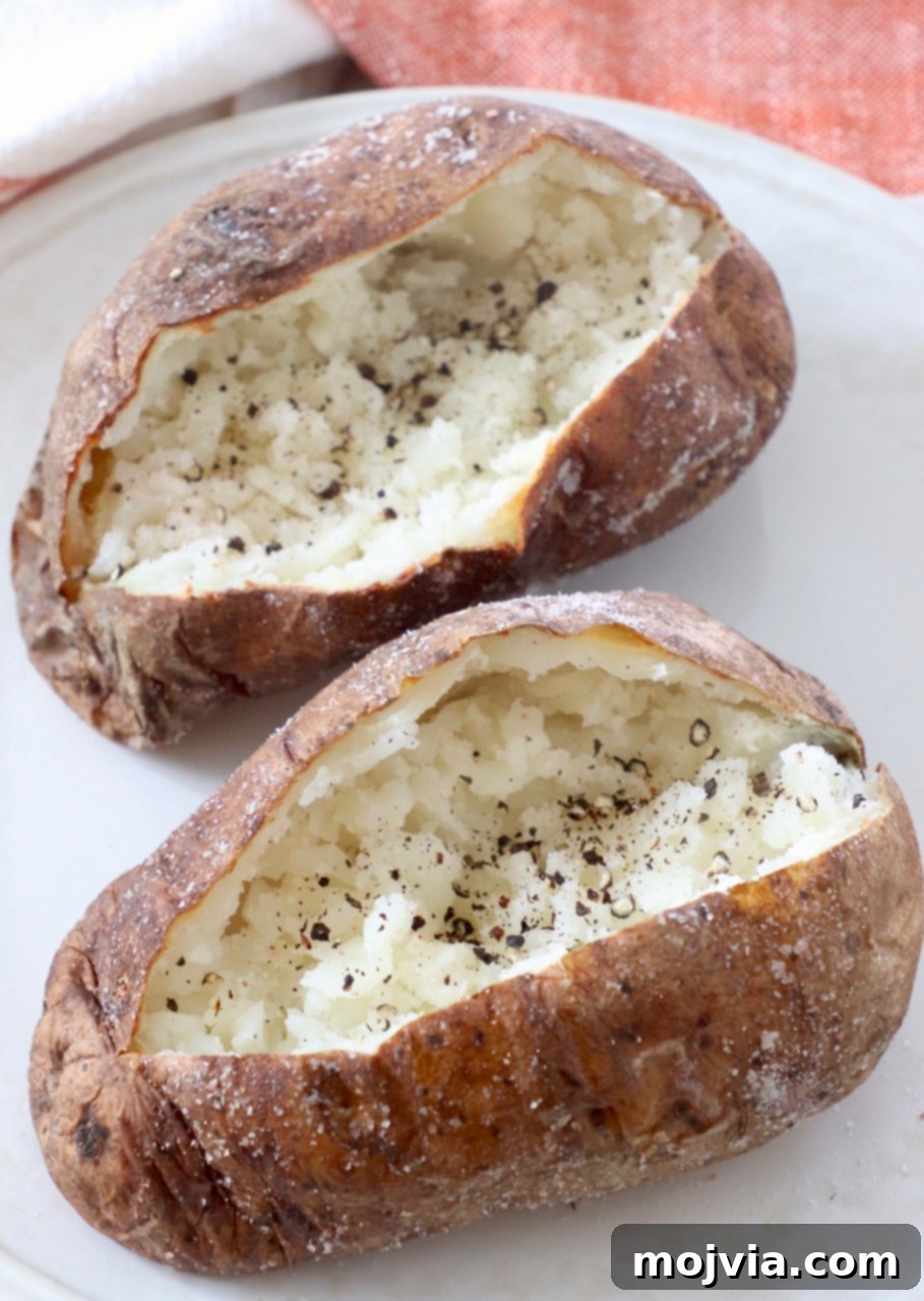 Crispy Air Fryer Baked Potatoes 6 sliced open baked potatoes on plate with black pepper sprinkled inside