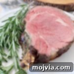 slice of bone-in prime rib on white plate with fresh rosemary sprigs