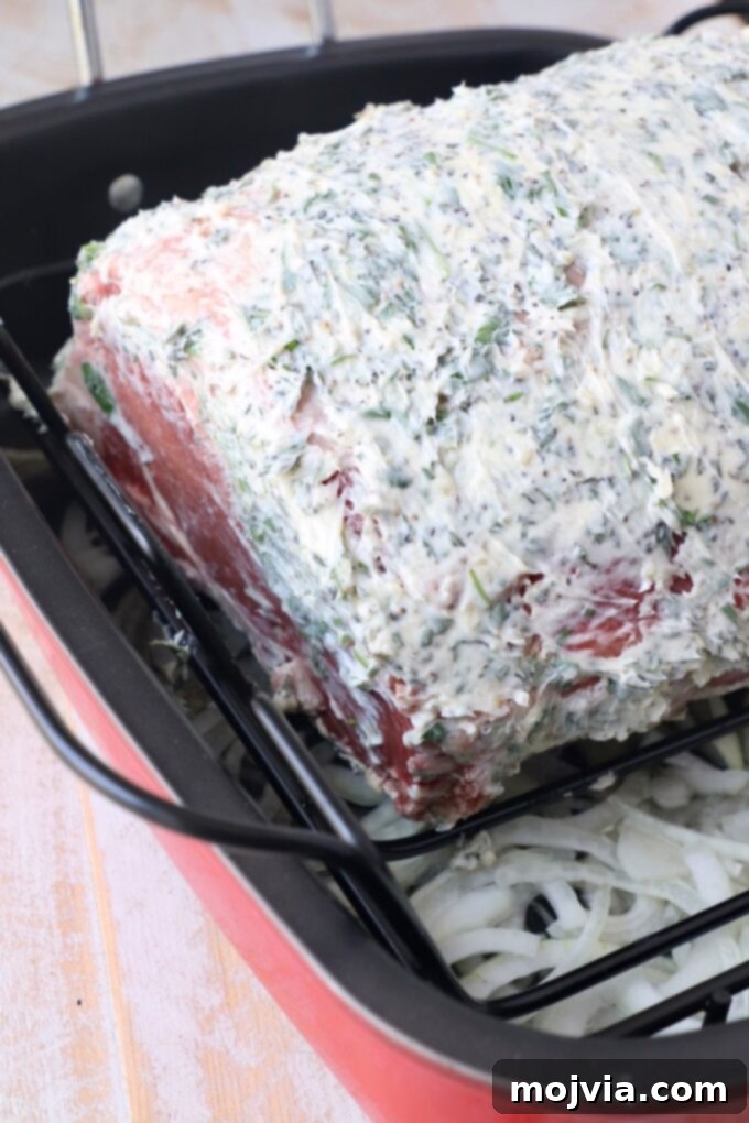 herb butter rubbed ribeye roast in roasting pan with sliced onions