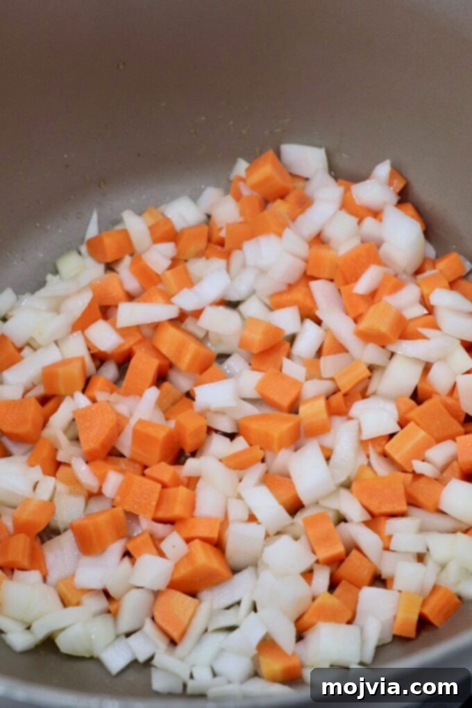 Golden Acorn Squash Comfort 5 Diced carrots and onions softening in a pot on the stove, building the flavor base for the soup.