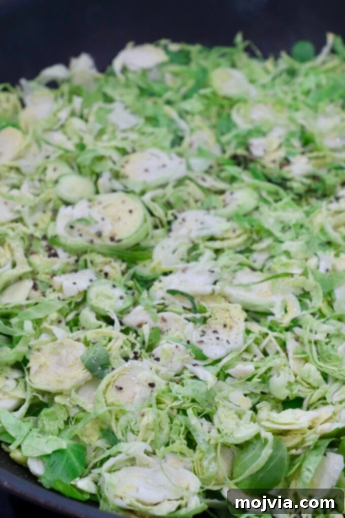 Shredded brussels sprouts and sliced shallots in a hot cast iron skillet with olive oil, just beginning to cook.