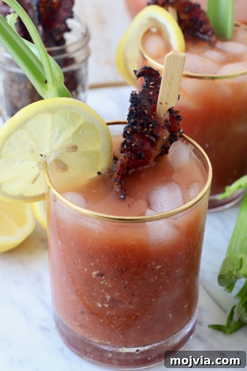Bloody Mary garnished with cooked bacon and a lemon slice in a tall glass