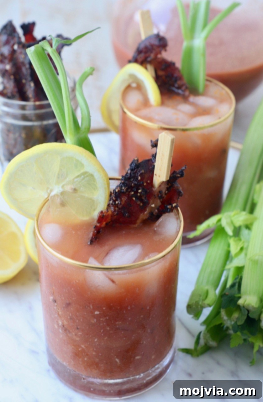 Two Bloody Mary cocktails in glasses, garnished with celery sticks, lemon slices, and crispy bacon