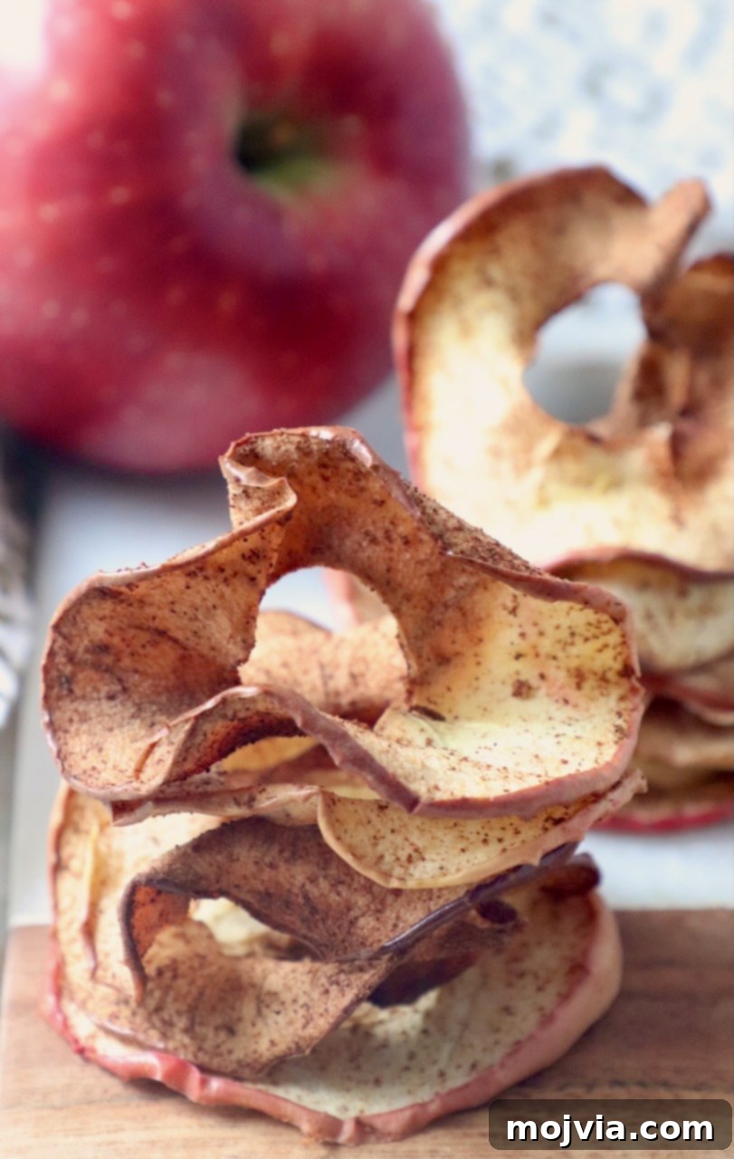 Crispy apple chips stacked on a cutting board next to a fresh whole apple, illustrating a healthy snack.