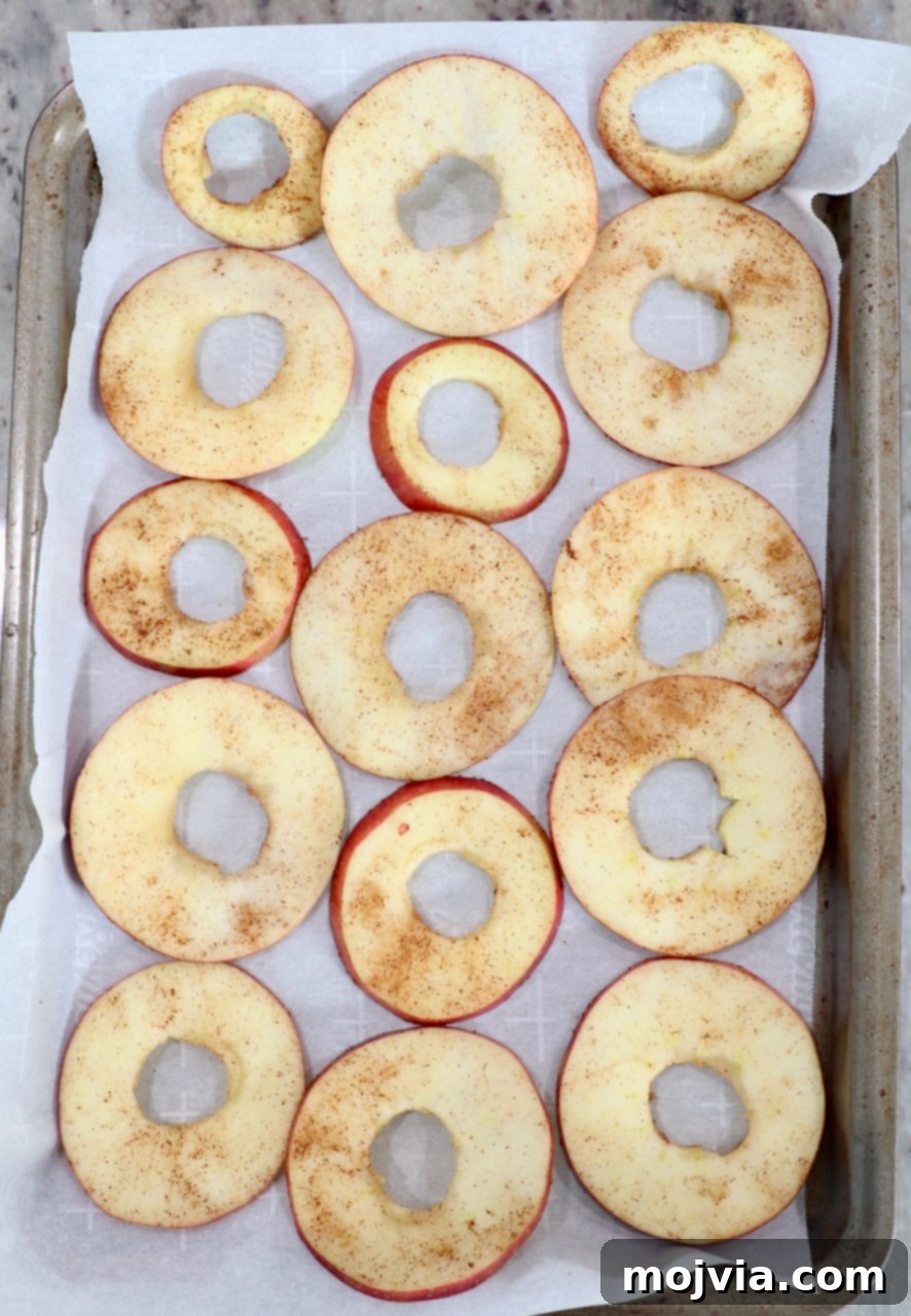 Thinly sliced apples dusted with cinnamon, laid out on a parchment-lined baking sheet, ready for the oven.