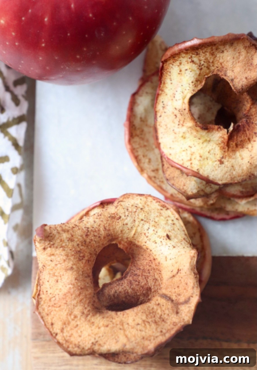 A stack of golden-brown apple chips on a wooden cutting board, showcasing their crisp texture.