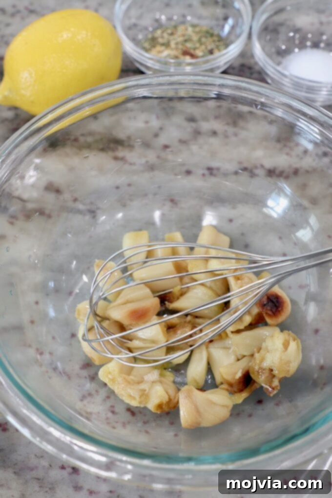 Sweet Roasted Garlic Spread 4 Roasted garlic cloves being mashed in a glass bowl with a whisk.