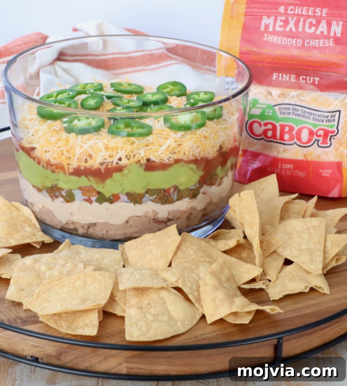 Sizzling Fajita Seven-Layer Dip 13 Fajita-Style 7 Layer Dip in a glass trifle bowl, surrounded by crispy tortilla chips on a large serving tray