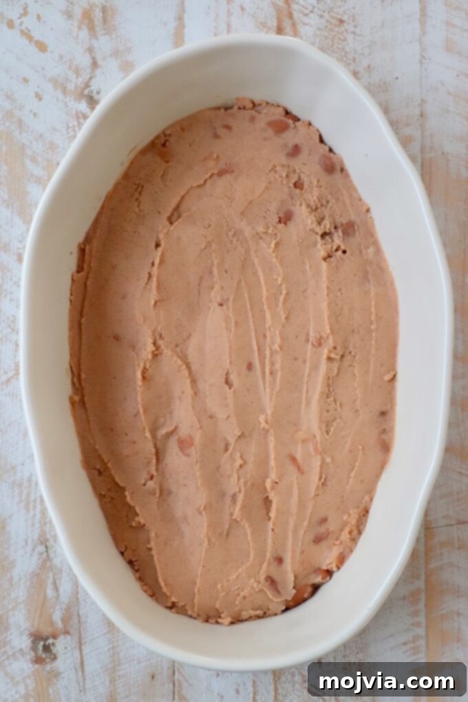 Sizzling Fajita Seven-Layer Dip 6 Refried beans spread as the first layer in a casserole dish