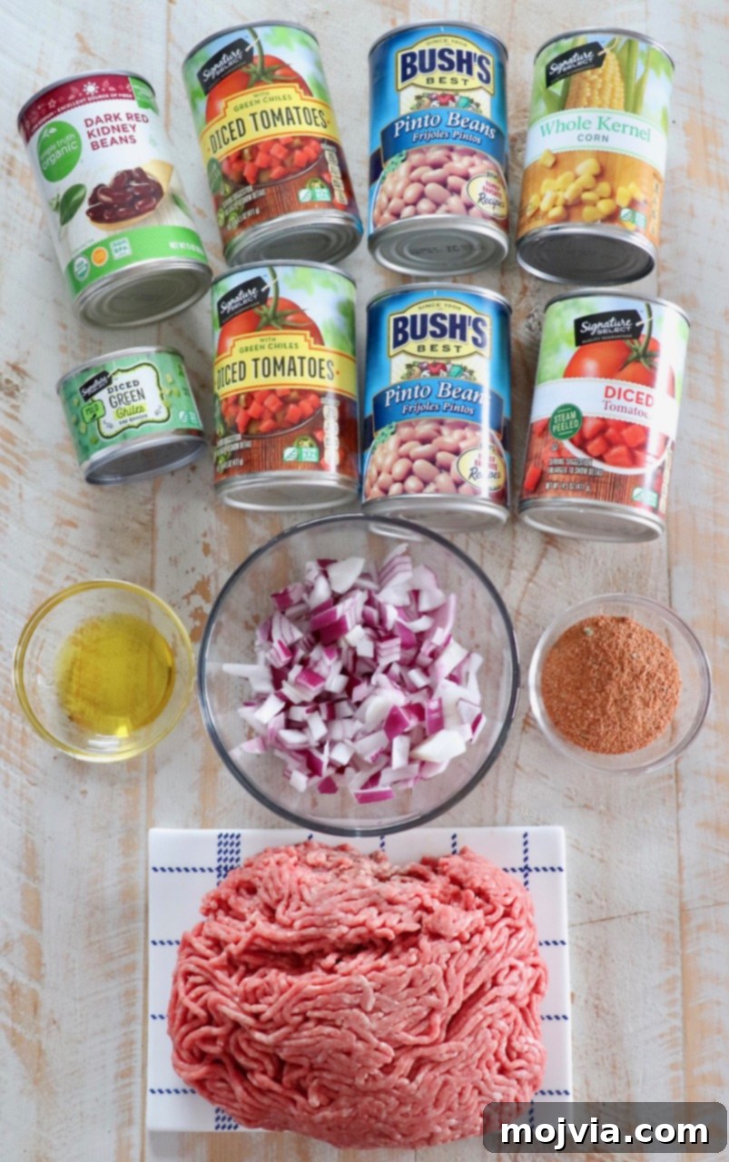 Arrangement of taco soup ingredients on a white wooden board, featuring cans of beans, tomatoes, corn, a bowl of diced onions, and ground beef, alongside an array of colorful spices.