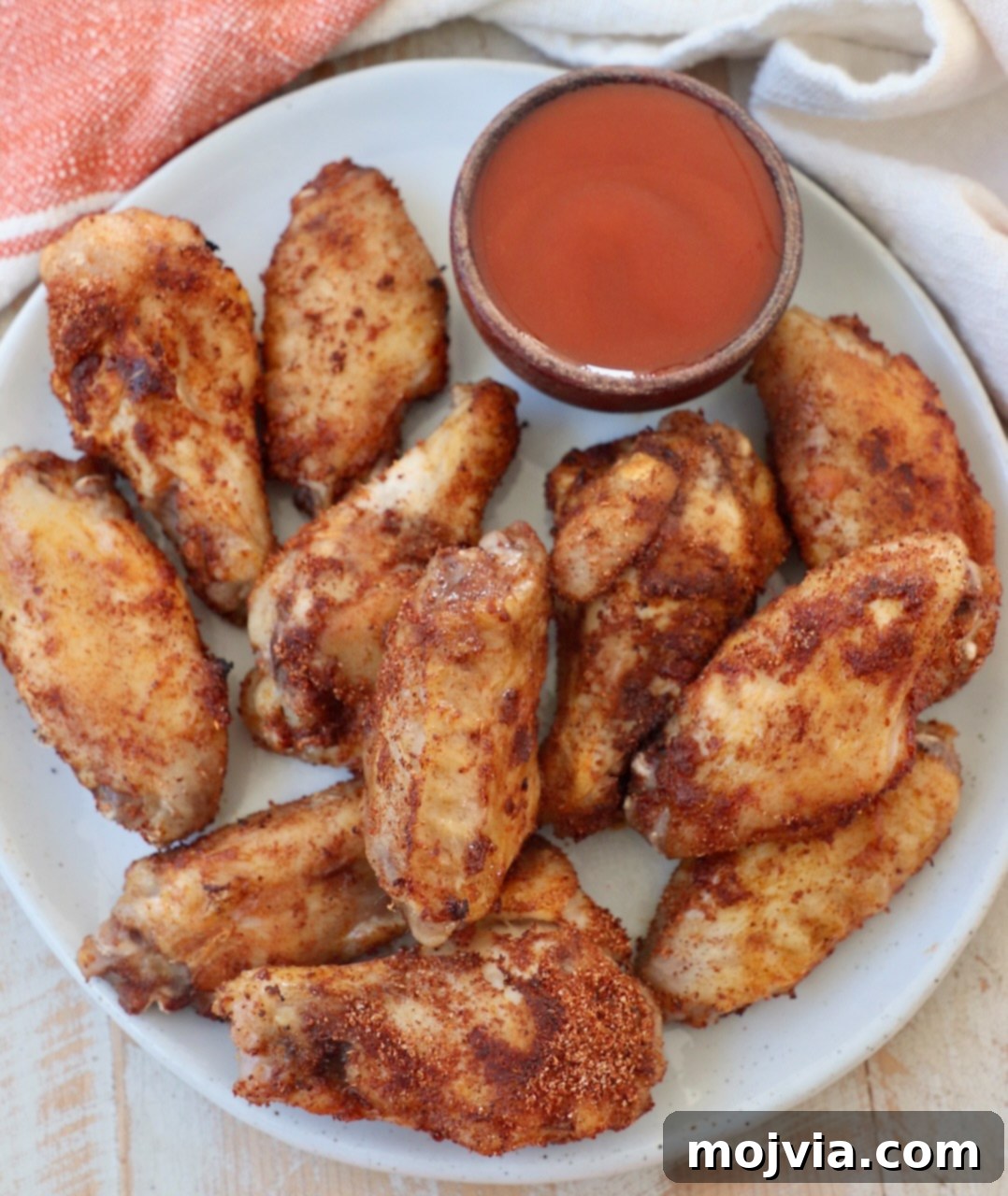 Sous Vide Wings: Crispy, Juicy Perfection 2 cooked chicken wings on plate with small bowl of buffalo sauce on the side