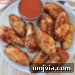 Sous Vide Wings: Crispy, Juicy Perfection 12 cooked chicken wings on plate with small bowl of buffalo sauce
