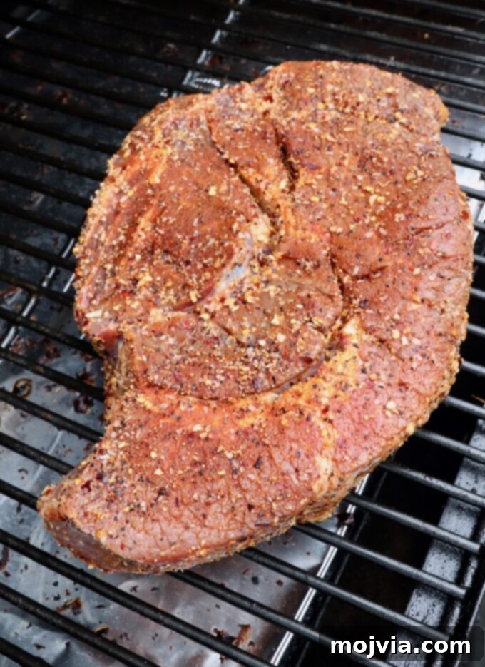 Seasoned chuck roast placed directly on the grates of a smoker, ready for the low and slow cooking process.