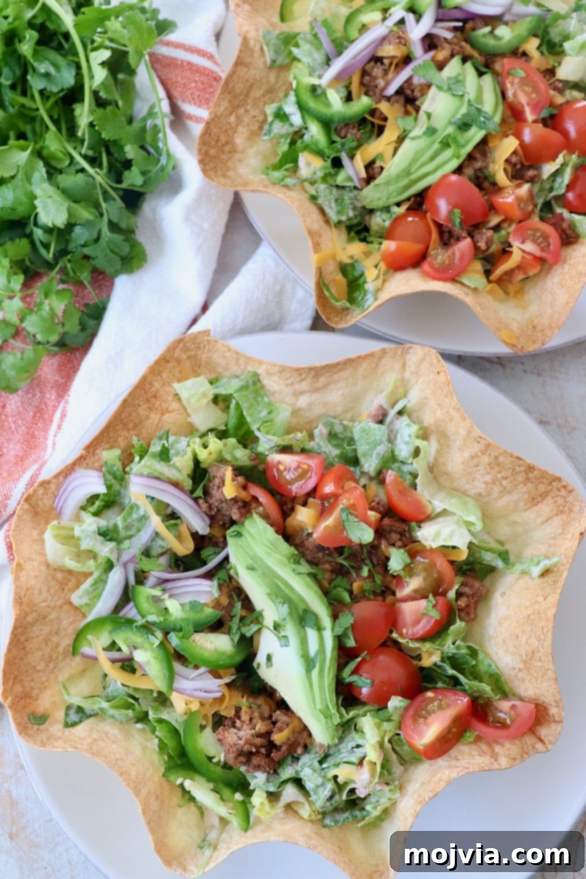 Hearty Beef Taco Salad 2 Vibrant taco salad in a golden tortilla shell bowl, generously topped with creamy sliced avocado, served on a pristine white plate.