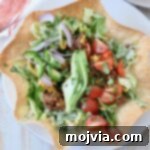 Taco salad in a tortilla shell on a plate, ready to be served.