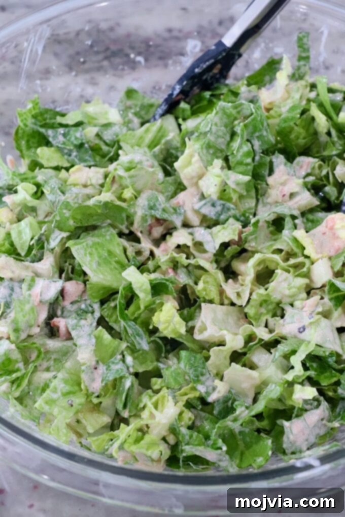 Hearty Beef Taco Salad 7 Crisp shredded lettuce being gently tossed with the homemade salsa and sour cream dressing in a large glass bowl, ensuring every leaf is coated.