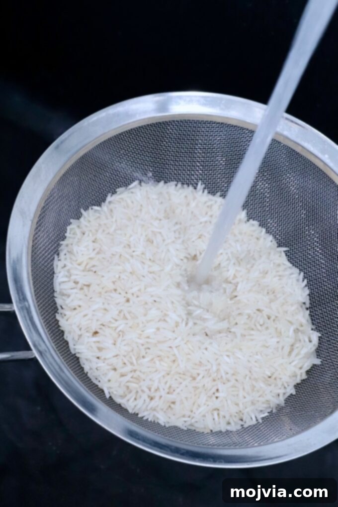 Fluffy Instant Pot Basmati Rice 3 white rice in mesh strainer in sink with water pouring over the rice